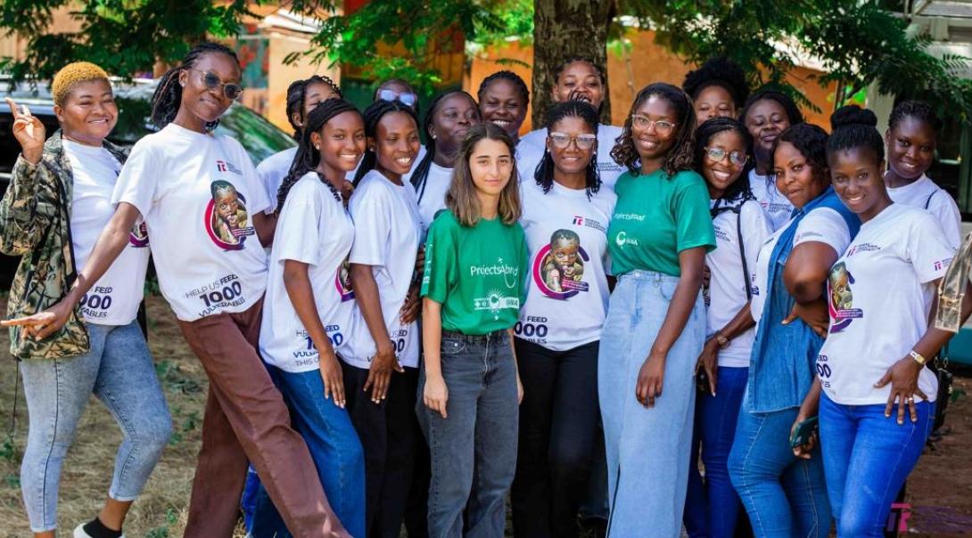 A group of women in Ghana smiling. Some are wearing Projects Abroad green t-shirts, while others are wearing shirts promoting a charity initiative to feed disadvantaged and vulnerable communities.