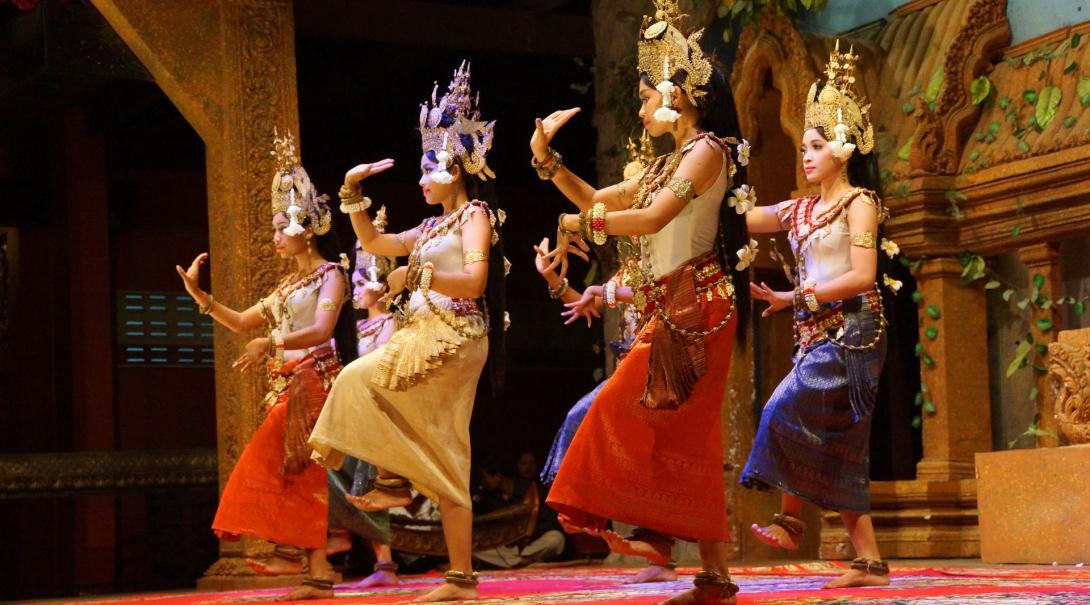 Six elegantly dressed women perform a traditional dance on stage 