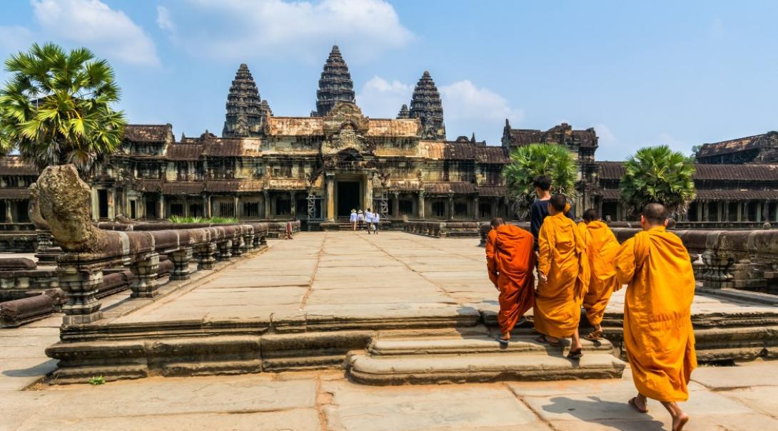 A group of 5 Buddhist monks walk on a large stone path towards the entrance of Angkor Wat