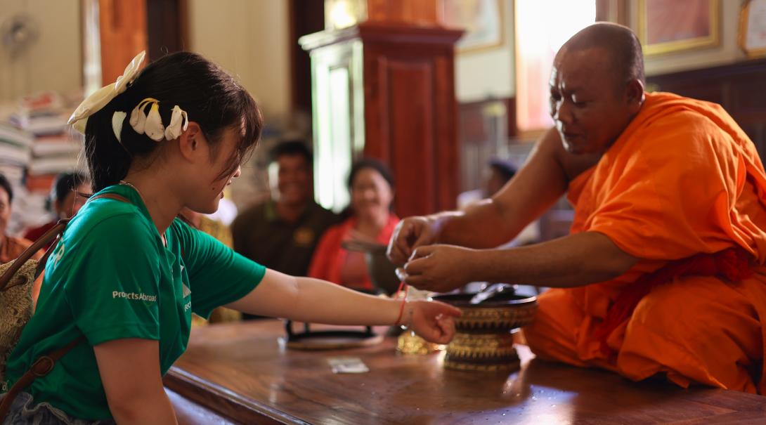 A Buddhist monk ties a red string around the wrist of a Projects Abroad volunteer 