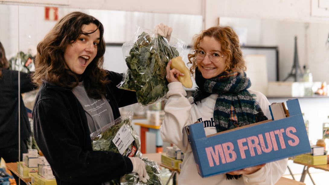 Two volunteers distribute fresh vegetables at a food distribution centre