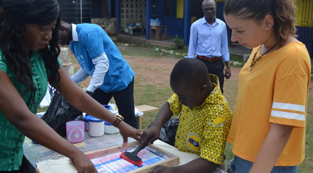 A gap year programs abroad volunteer helps a teacher and child in Ghana with an art project.