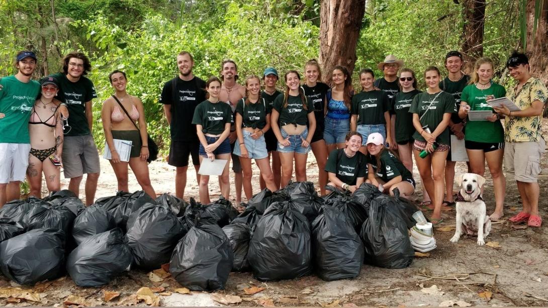 A large group of Projects Abroad volunteers stand behind a huge pile of rubbish that they collected on a beach clean in Thailand.