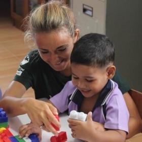 Voluntaria social ayudando a un niño a jugar con bloques en un centro de cuidado tailandés.