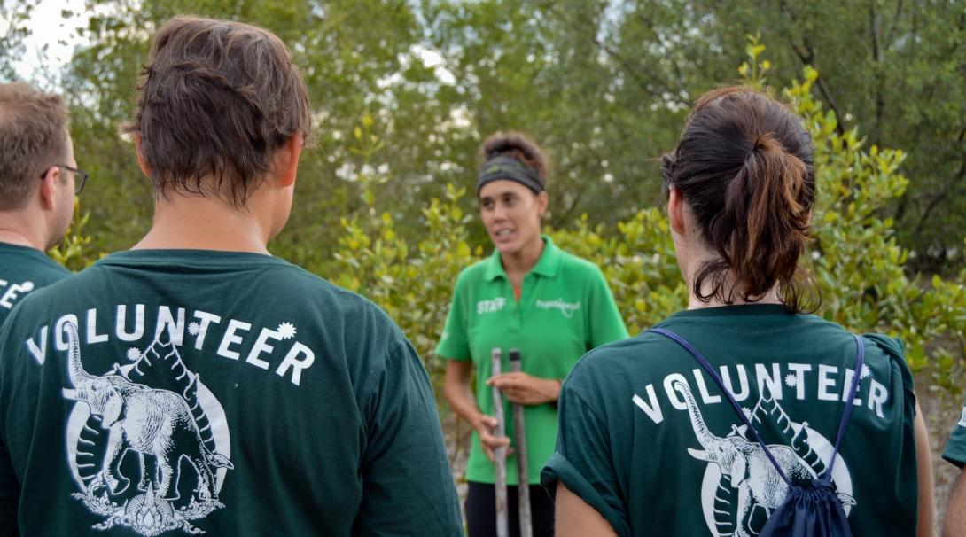 A group of Projects Abroad Conservation volunteers listen to a staff member explain an activity outdoors at their project. 