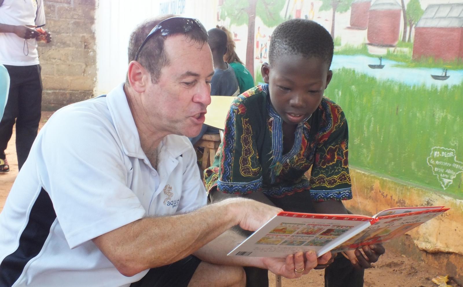 An older volunteer reads to a child as part of his childcare volunteer work overseas