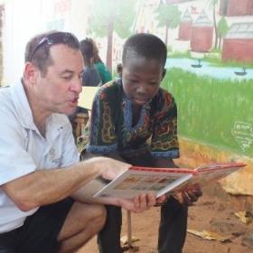 An older volunteer reads to a child as part of his childcare volunteer work overseas