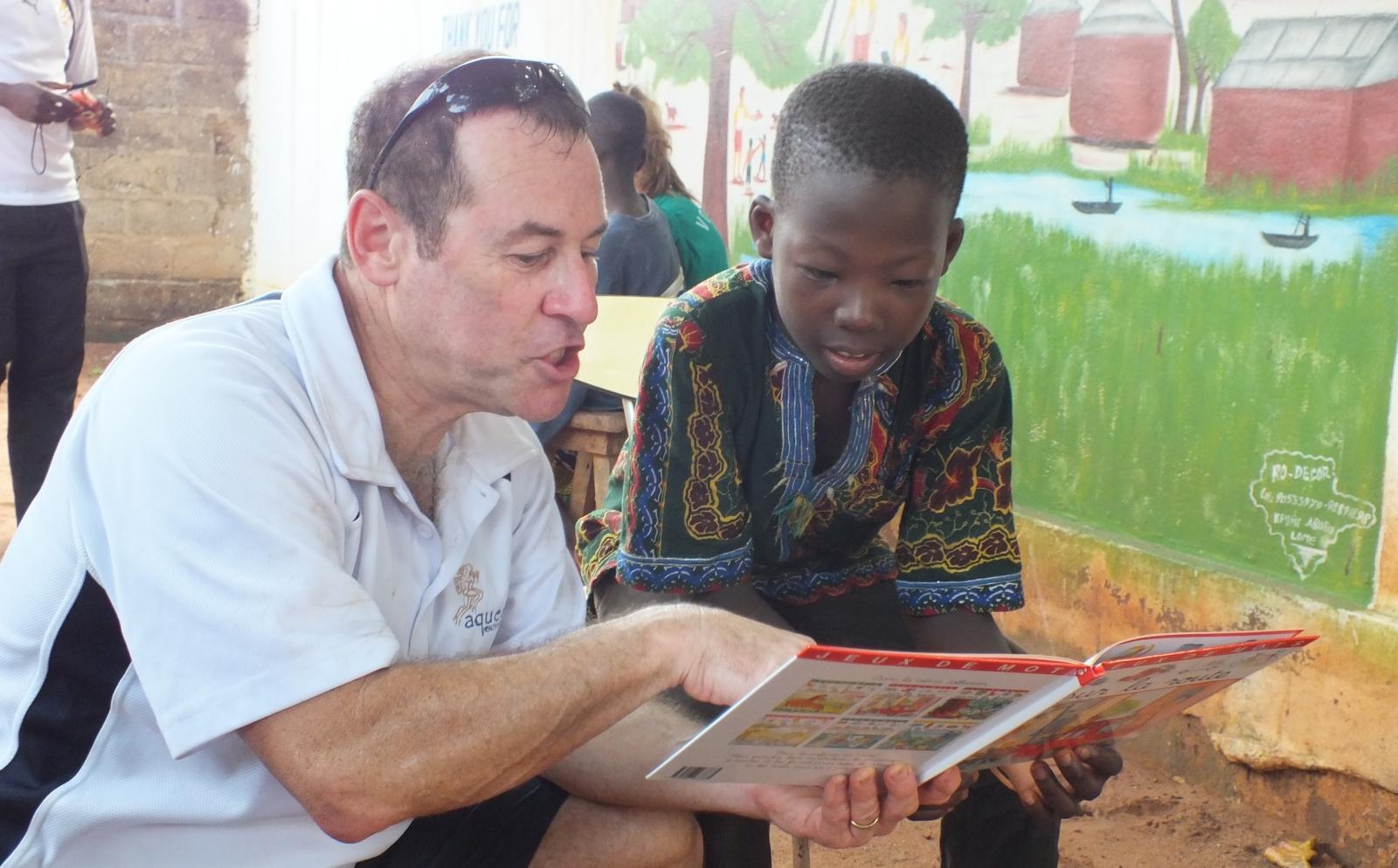 An older volunteer reads to a child as part of his childcare volunteer work overseas