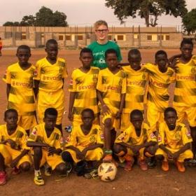 Een jonge vrijwilliger poseert met zijn leerlingen tijdens zijn sport vrijwilligersproject in Ghana.