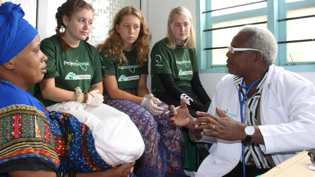 Medical interns in Tanzania listen to a doctor during a consultation with a woman