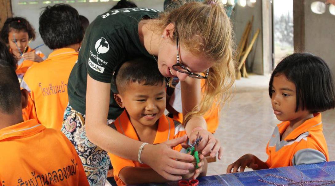 On an ethical volunteering opportunity, a Childcare volunteer in Thailand assists children during an arts and craft session.