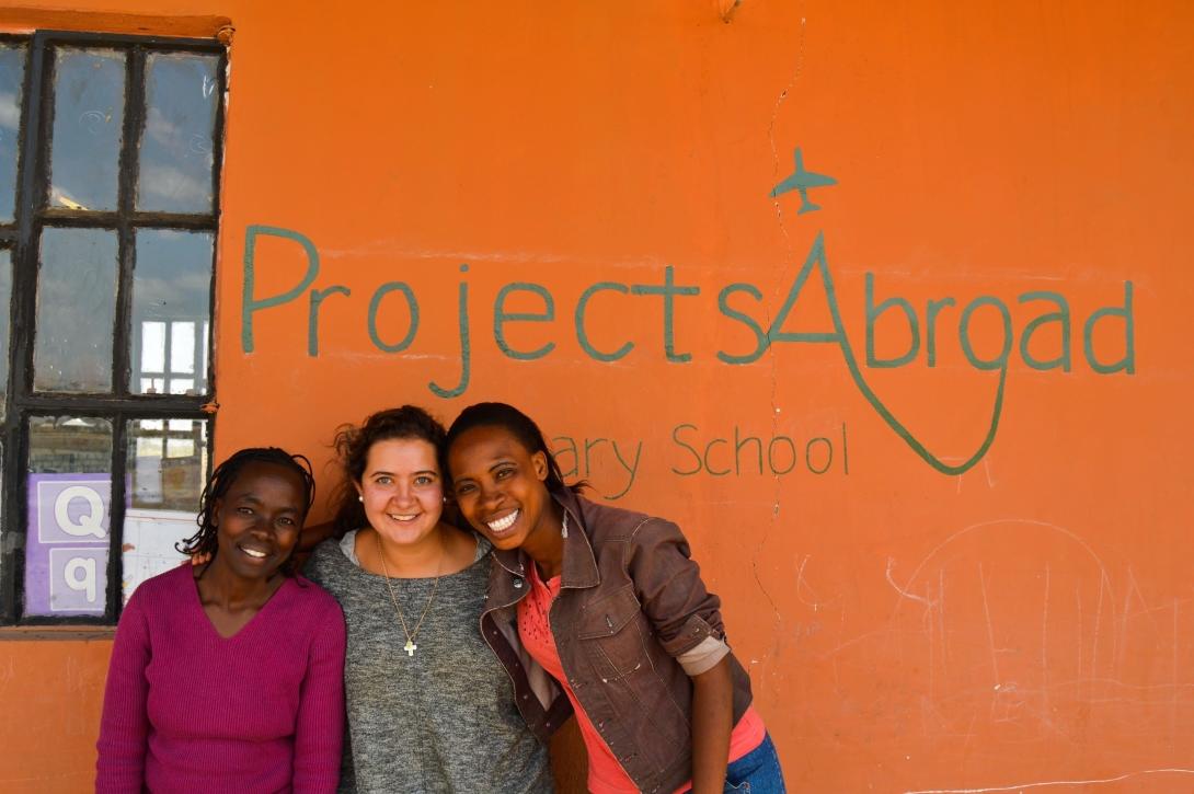 En volontär poserar utanför med personal från en skola som Projects Abroad byggt.
