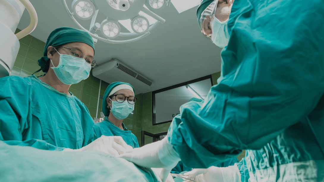 Three medical professionals wearing scrubs lean over a table in the operating theatre